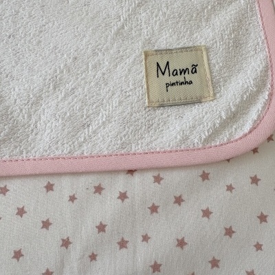Toalha branca com borda rosa e etiqueta com texto, sobre tecido com estrelas rosa