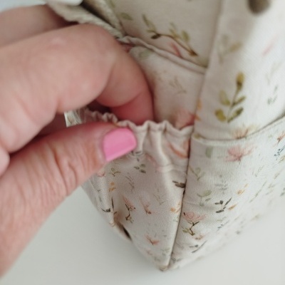Bolsa com padrão floral e bolso elástico sendo tocado por mão com unha rosa