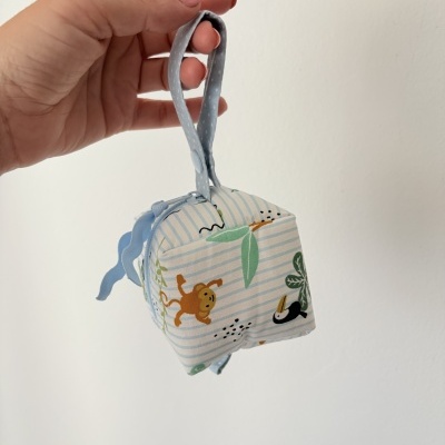 Cubo de tecido infantil com padrão de macacos e folhas, alça azul, segurado por mão em fundo branco
