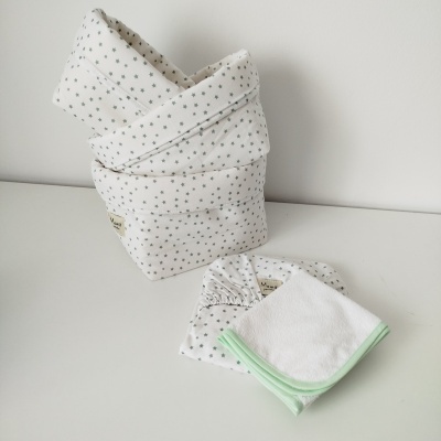 Conjunto para bebé com cesto de tecido e fralda numa superfície branca.