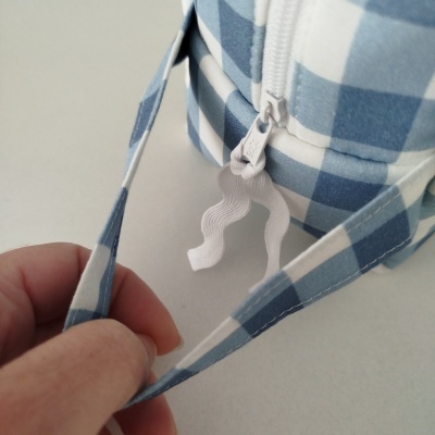 Fecho de correr branco num saco com padrão de quadrados azuis e brancos, com alça do mesmo tecido a ser segurada.