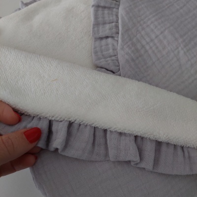 Toalha branca texturizada sobre tecido cinza com folhos e mão com unhas vermelhas.