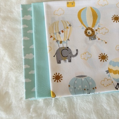 Três tecidos dobrados com padrões de balões, animais e nuvens sobre superfície branca felpuda.