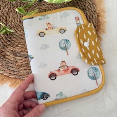 Capa em tecido com padrão de carros e animais, borda amarela, fecho em tecido amarelo com padrões brancos.