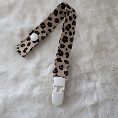 Tira para chupeta com padrão animal print e fecho branco sobre superfície peluda branca