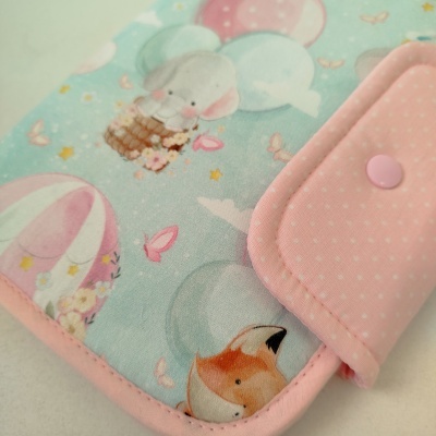 Capa de tecido com padrão de balões e animais, acabamento cor-de-rosa com botões.