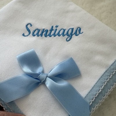 Fralda branca bordada com o nome Santiago em azul com laço azul claro.