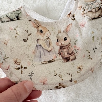 Bavoir infantil com padrão de coelhos e fundo creme com flores.