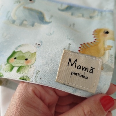 Tecido com padrão de dinossauros e etiqueta com texto Mamã pintinha