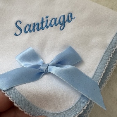 Fralda branca bordada com o nome Santiago em azul e laço azul.