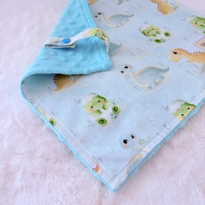 Manta ou toalha infantil azul com estampado de dinossauros e verso azul em textura aveludada