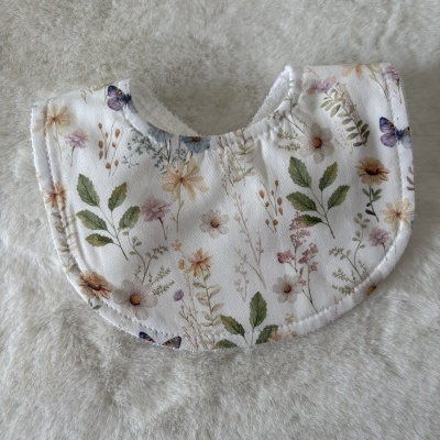 Babete de bebé redondo com padrão floral e borboletas em tecido branco