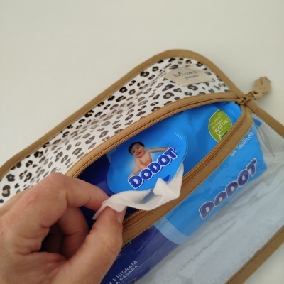 Bolsa castanha com padrão animal print com pack azul de toalhitas Dodot e mão a puxar uma toalhita branca
