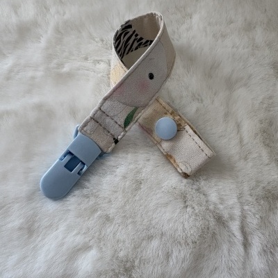Prendedor para chupeta em tecido bege com padrão floral e botão azul