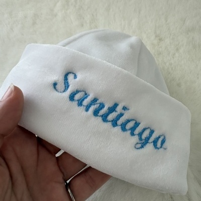 Chapéu branco com bordado azul Santiago num fundo branco texturizado
