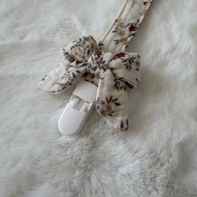 Tira com padrão de flores pequenas e clip branco numa superfície felpuda cinza