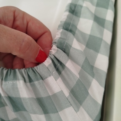 Pano xadrez branco e verde claro com elástico, segurado por uma mão com unhas vermelhas.