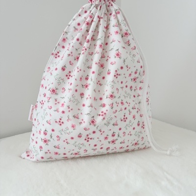Saco de tecido branco com padrão floral rosa e cordão branco numa superfície branca
