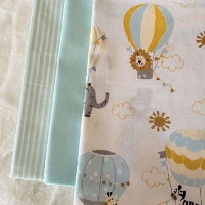 Três tecidos dobrados com estampados de animais e balões coloridos, azul claro e riscas verticais azuis