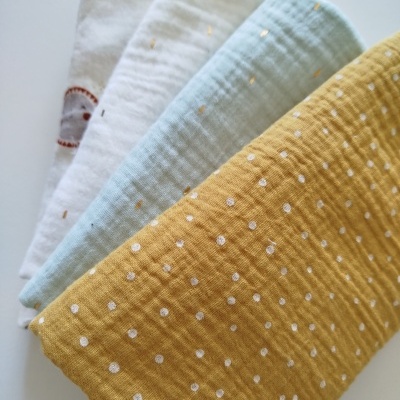 Quatro panos de algodão em branco, azul claro e amarelo com padrões de pontos, em superfície branca