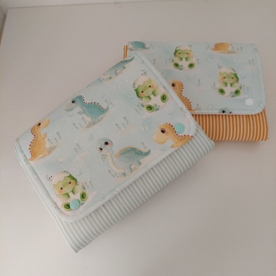 Duas carteiras com estampado de dinossauros e listras, uma azul e outra amarela, com fecho de botão.