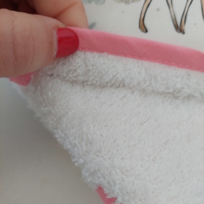 Toalha branca com borda rosa sendo segurada por mão com unha vermelha
