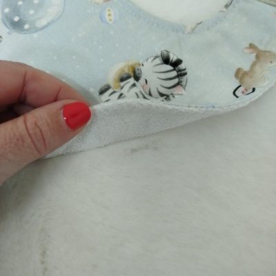 Babeiro azul claro com desenhos de zebra e coelho, tecido macio branco no reverso.