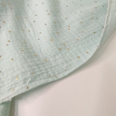 Tecido azul claro com pontos dourados sobre superfície branca