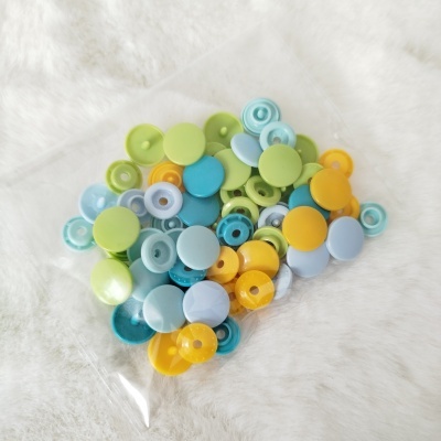 Botões de pressão coloridos em pacote transparente sobre superfície branca.