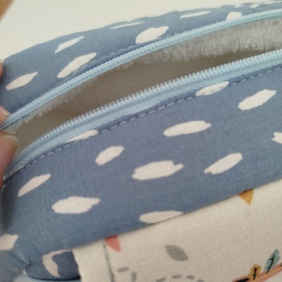 Estojo de tecido azul com manchas brancas e fecho de zipper azul claro aberto mostrando interior felpudo branco