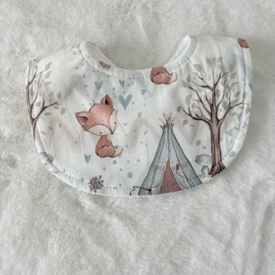 Babete de tecido com estampado de raposa e natureza sentada em fundo felpudo branco