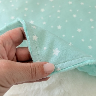 Tecido azul claro com estrelas brancas segurado por mão, sobre superfície branca felpuda