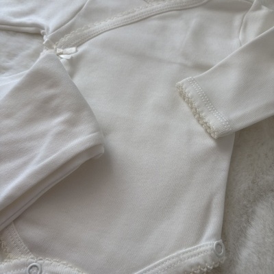Body e calças de bebé em algodão branco com renda delicada e botões de pressão.