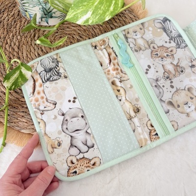 Carteira com padrão de animais bebés e fecho verde menta aberta sobre fundo branco peludo