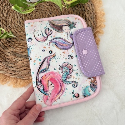 Estojo de tecido com padrão de sereias em cores pastel e fecho lilás com pontos brancos.