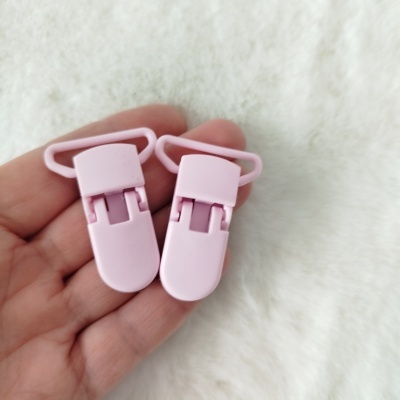 Dois clips de plástico rosa claro em mãos sobre fundo branco.