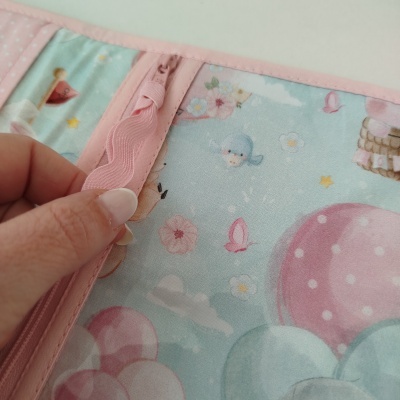 Organizador em tecido colorido com padrão de balões, flores e pássaros, costura e fecho rosa aberto por mão