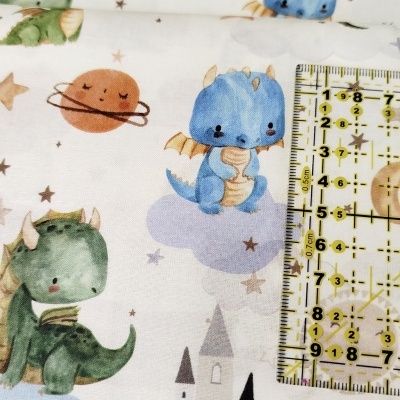 Tecido infantil com padrão de dragões, planetas e castelo junto a régua