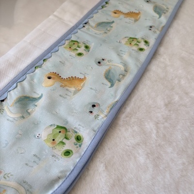 Proteção azul claro com estampa de dinossauros e borda azul sobre superfície branca acolchoada