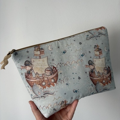 Bolsa de tecido azul claro estampada com navios e personagens, segurada por uma mão.