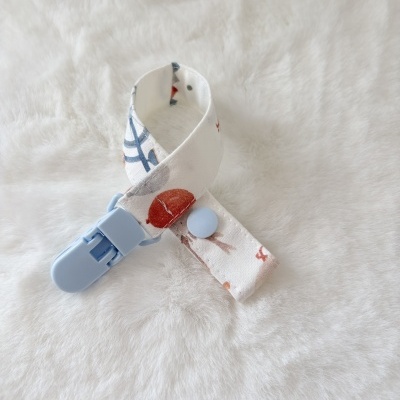 Clips para chupeta com tecido estampado, botão e clipe azul claro sobre tecido branco macio