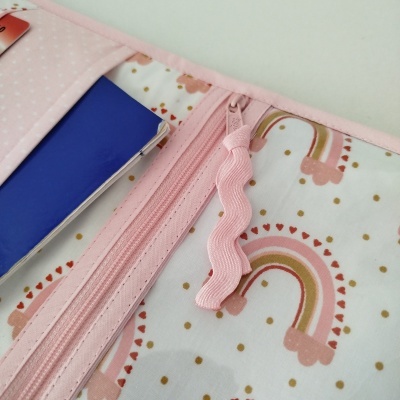 Estojo de tecido branco com padrões de arco-íris cor-de-rosa e bege, fecho rosa e bolsos interiores com cadernos azuis