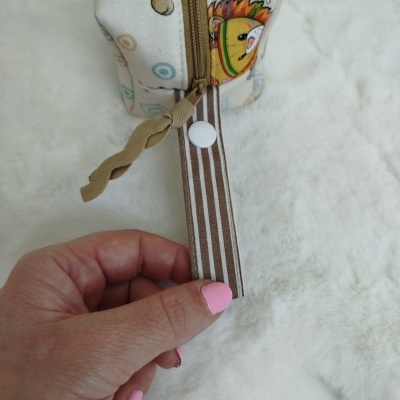 Bolsa pequena com tecido estampado, etiqueta às riscas castanhas e brancas e mão segurando a etiqueta