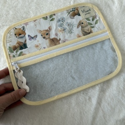 Estojo transparente com borda amarela e fecho branco, parte superior com desenho de animais e flores