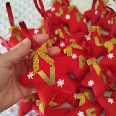 Decorações em forma de estrela vermelha com letras douradas e flores brancas, penduradas em fitas vermelhas.