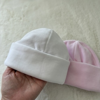 Dois chapéus de bebé, um branco e outro cor-de-rosa, em tecido macio sobre uma superfície felpuda clara