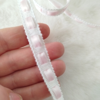 Fita decorativa fina branca e rosa claro com textura macia sobre fundo felpudo branco