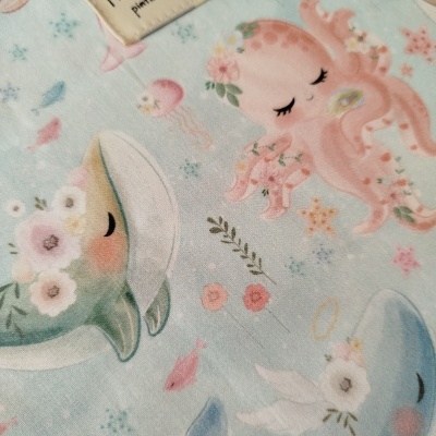 Tecido azul claro com padrão de animais marinhos e etiqueta 'Mamá pintinha'