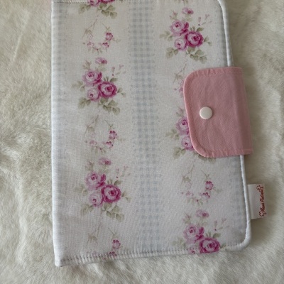 Estojo floral em tecido com fecho rosa e botão branco sobre fundo beige.