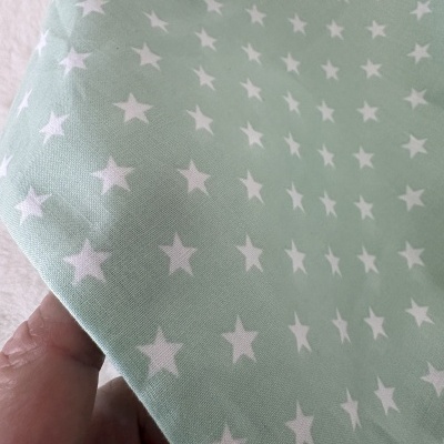 Pano de tecido verde-água com estrelas brancas e textura de algodão sendo segurado por mão.